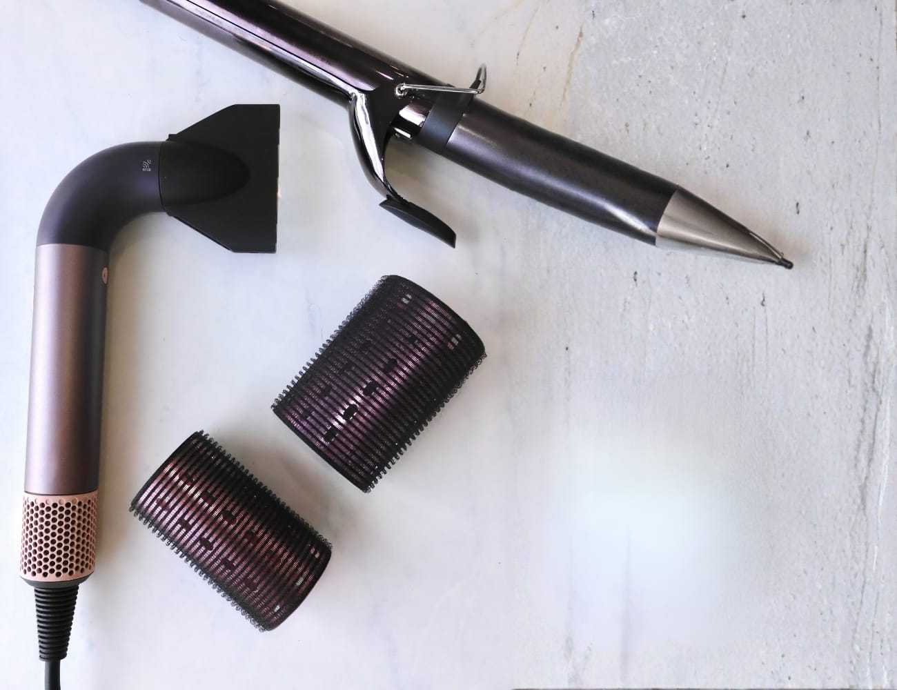 Hair styling tools on a countertop, including a hairdryer, curling iron, and two rollers.