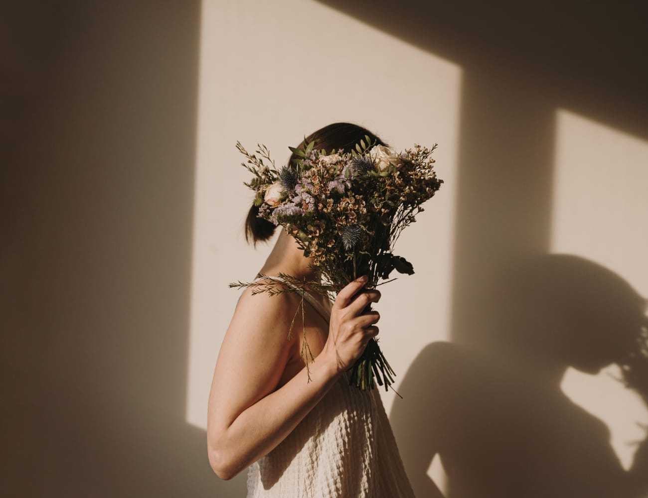 A person holding a bouquet of flowers, face obscured by shadows on a wall.