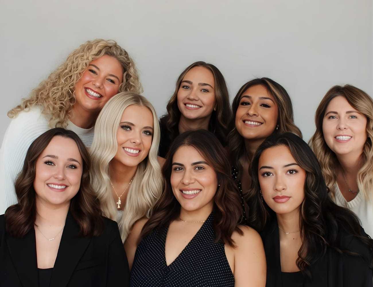 Group of eight smiling women posing against a neutral background.
