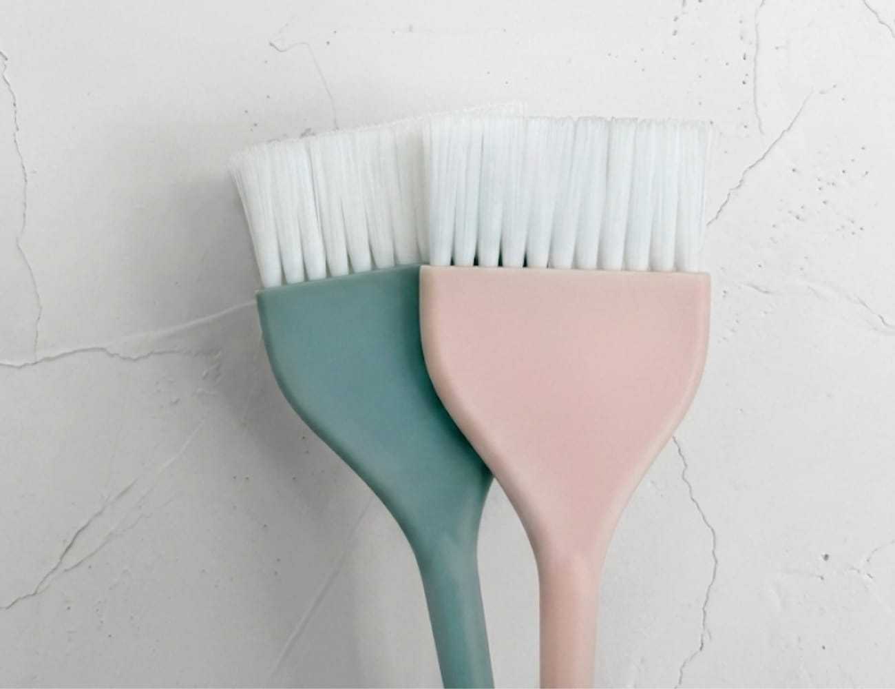 Two pastel-colored paintbrushes with white bristles on a marble surface.